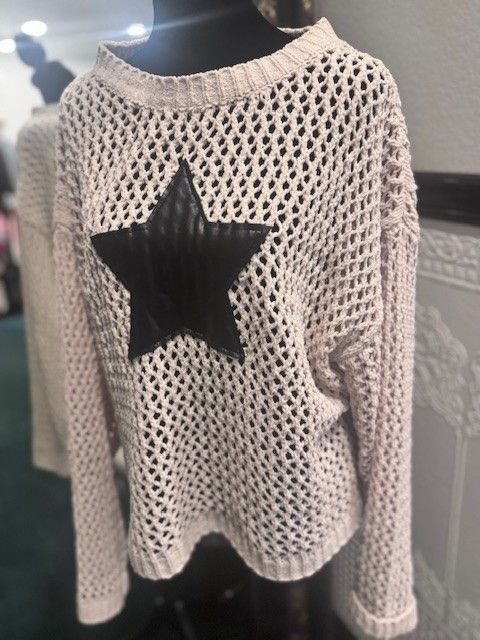 A white sweater with a black star on the back is on a mannequin.