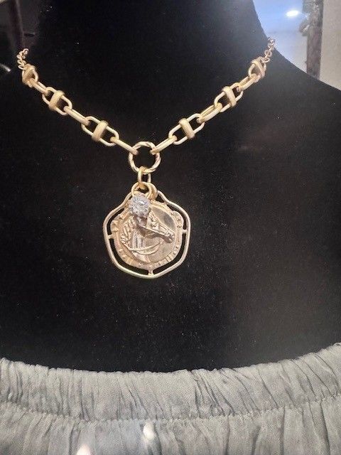 A woman wearing a gold necklace with a coin pendant