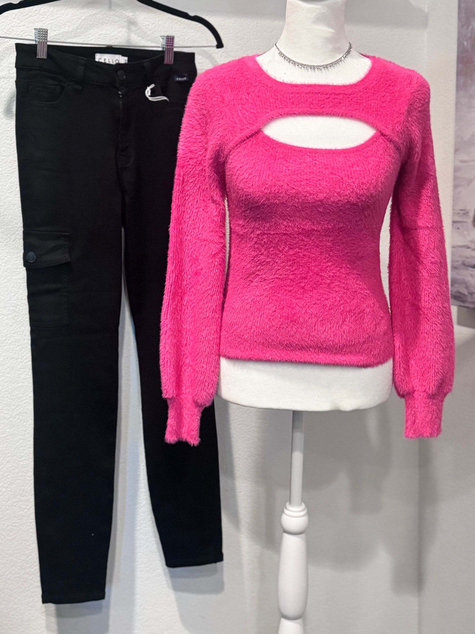 A pink sweater and black pants are on a mannequin.