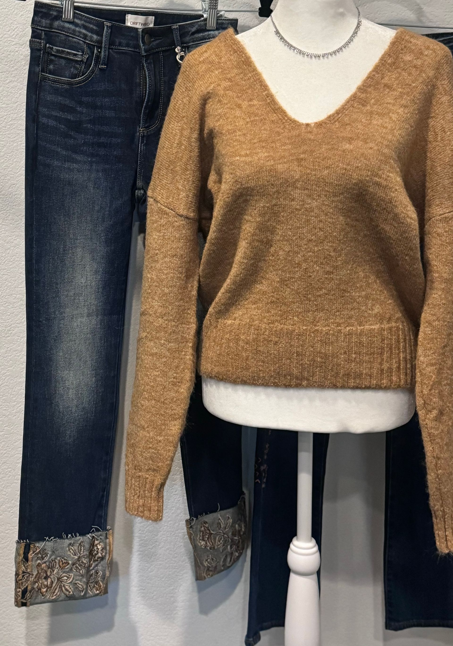 A mannequin is wearing a brown sweater and blue jeans.