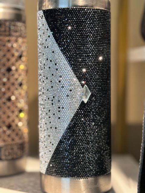 A stainless steel water bottle with rhinestones on it is sitting on a table.