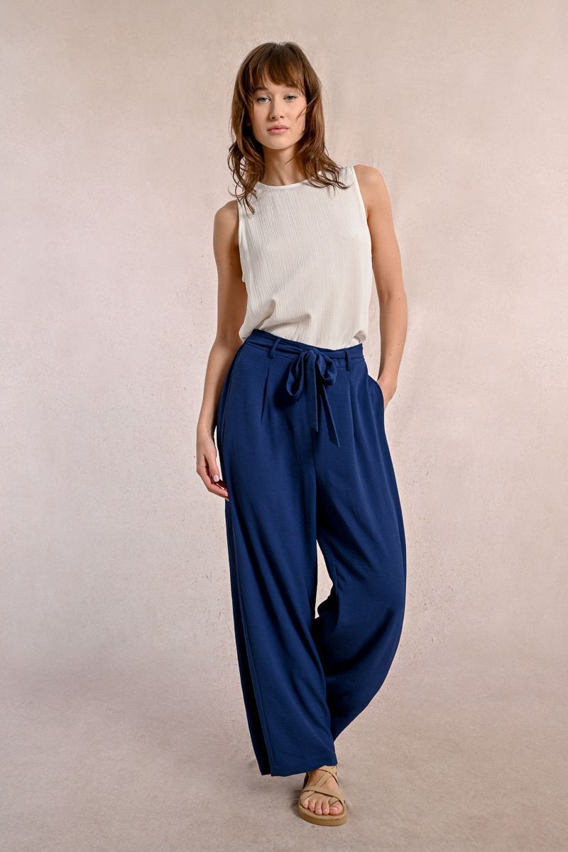 A woman is wearing a white tank top and blue pants.