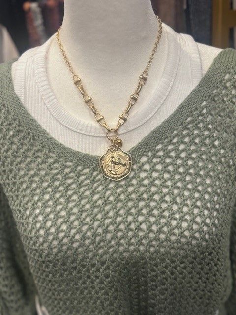 A woman wearing a green sweater and a gold necklace with a coin pendant.