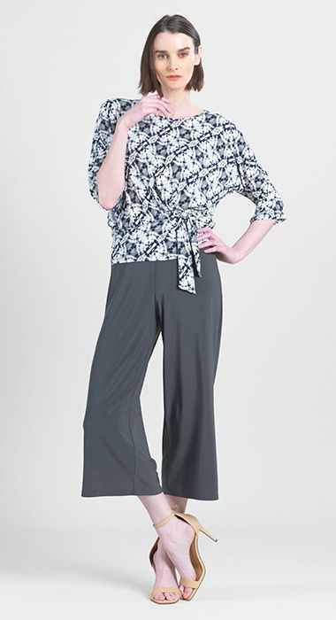 A woman is wearing a floral top and wide leg pants.