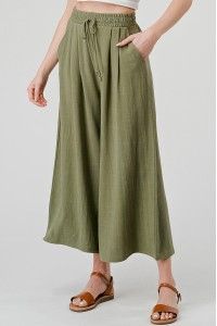 A woman is wearing a white crop top and green culottes.
