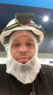 A man wearing a hard hat and a hood is looking at the camera.