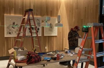 Two men are working on a wooden wall in a room with ladders.
