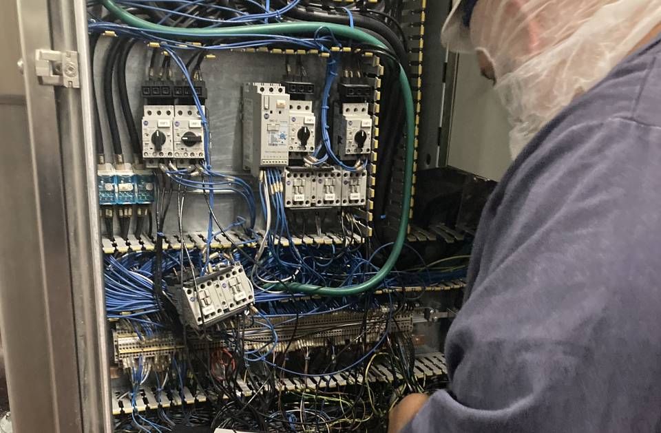 A man in a blue shirt is working on a electrical box.