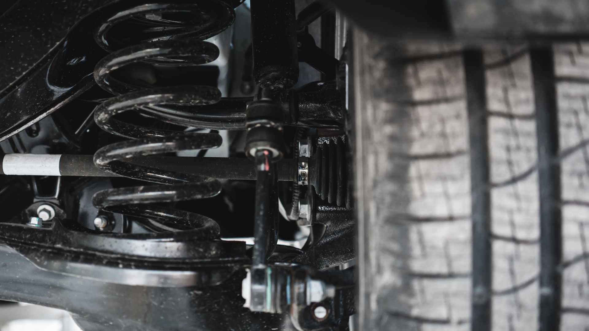 Close-up of a vehicle’s suspension and tire tread, showing the wheel well and coil spring.