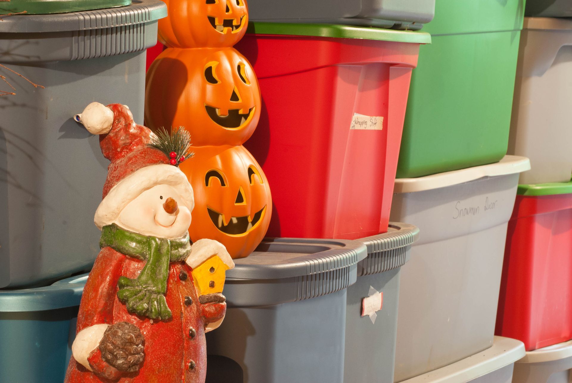 A stack of plastic bins with pumpkins and a snowman on top of them.