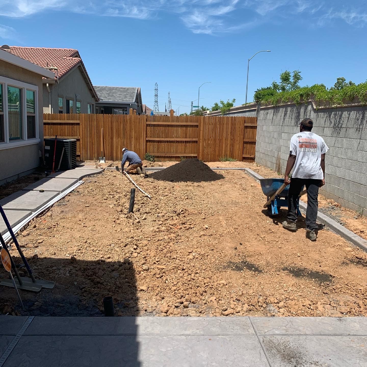 A man is pushing a wheelbarrow in a dirt yard