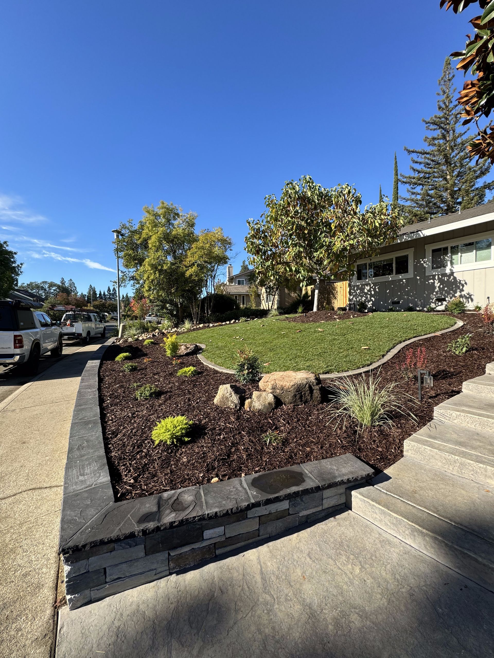 A house with a lush green lawn and a brick wall in front of it.