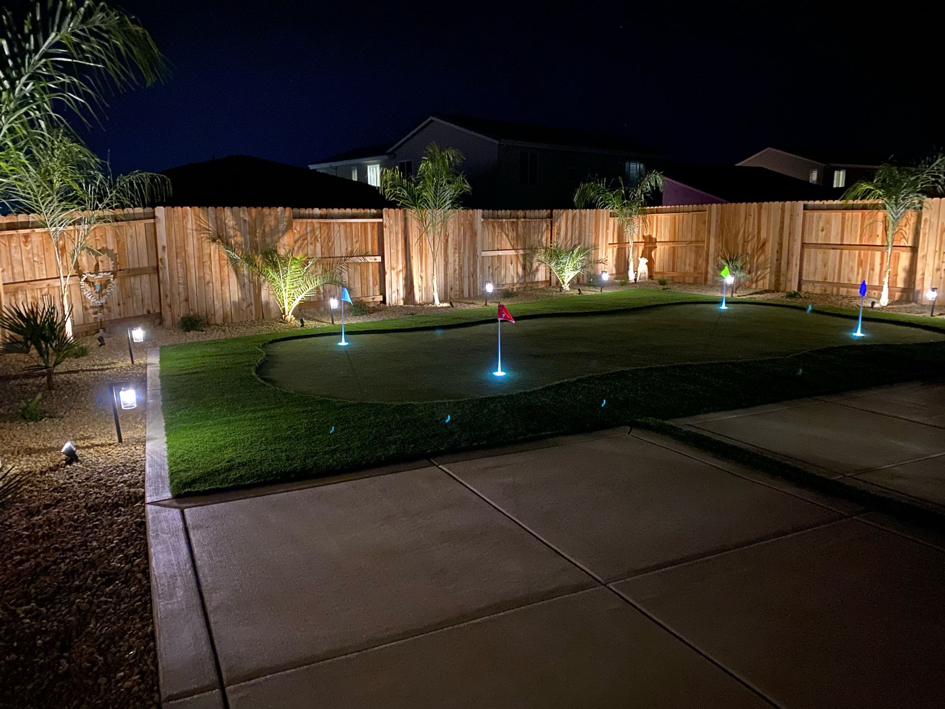 A backyard with a putting green and a wooden fence at night.