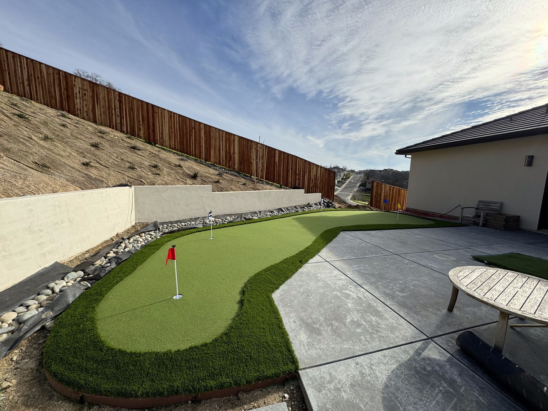 There is a small putting green in the backyard of a house.