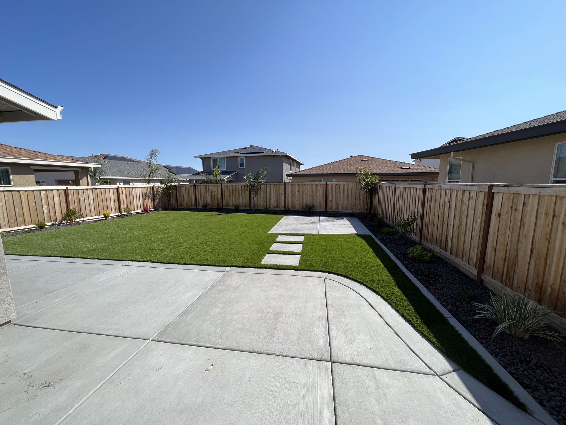 A backyard with a wooden fence and a concrete walkway