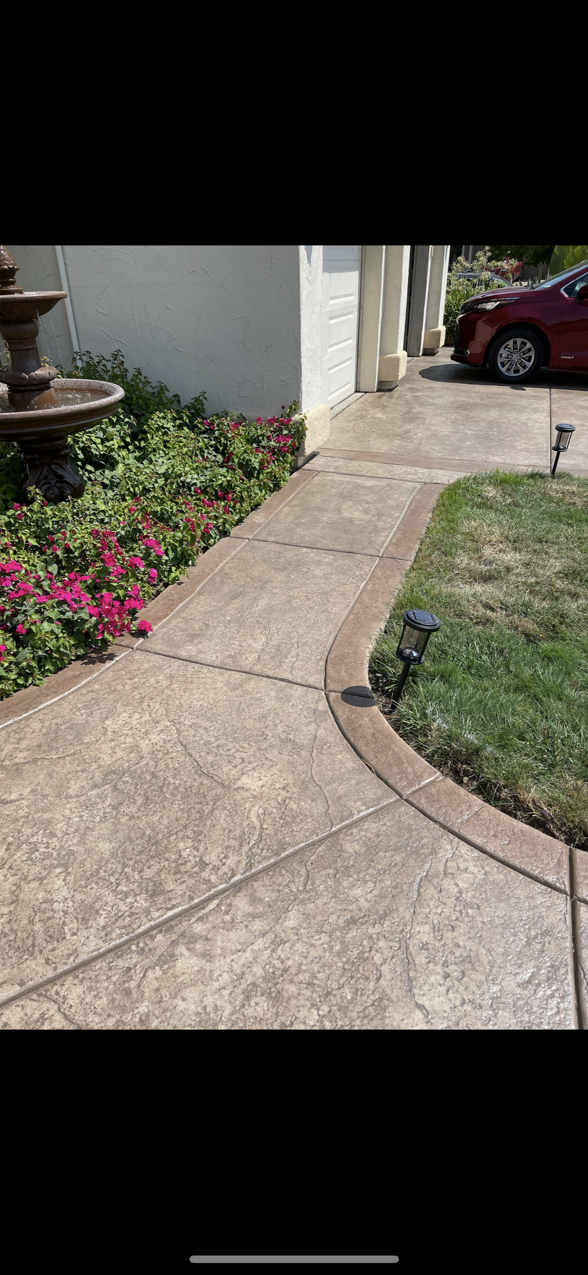 A concrete walkway leading to a house with a red car parked in the driveway.