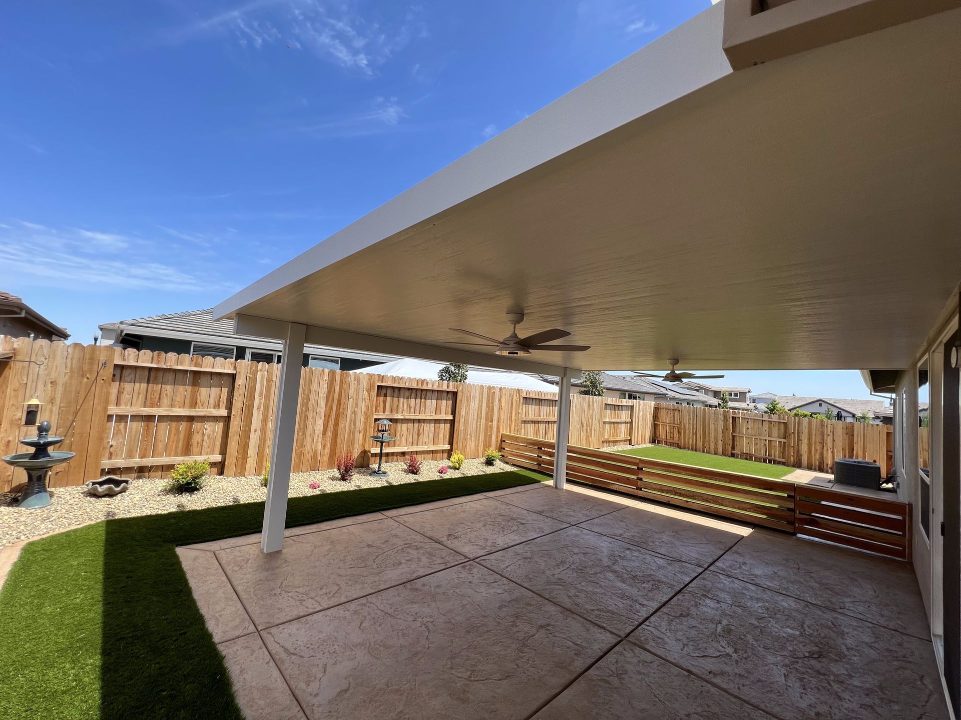 A patio with a ceiling fan and a wooden fence in the background.