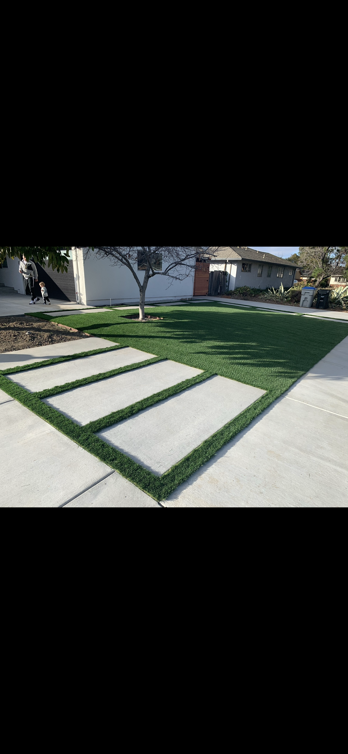 A lawn with a concrete walkway leading to it and a house in the background.