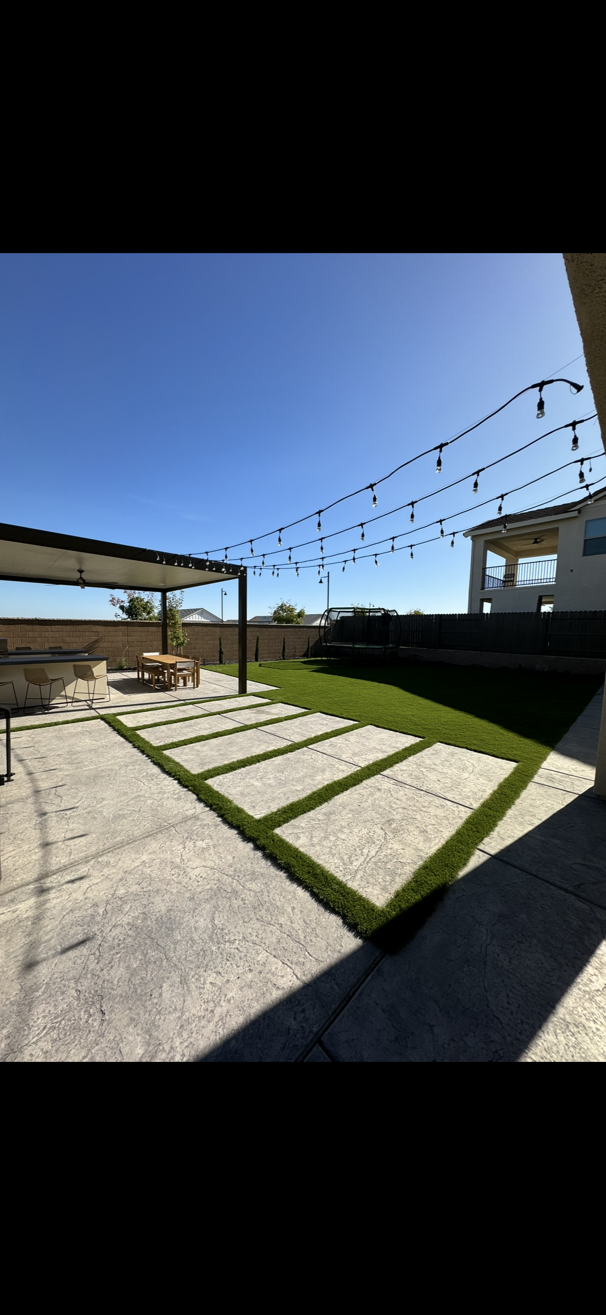 A patio with a pergola and a lawn in front of a house.