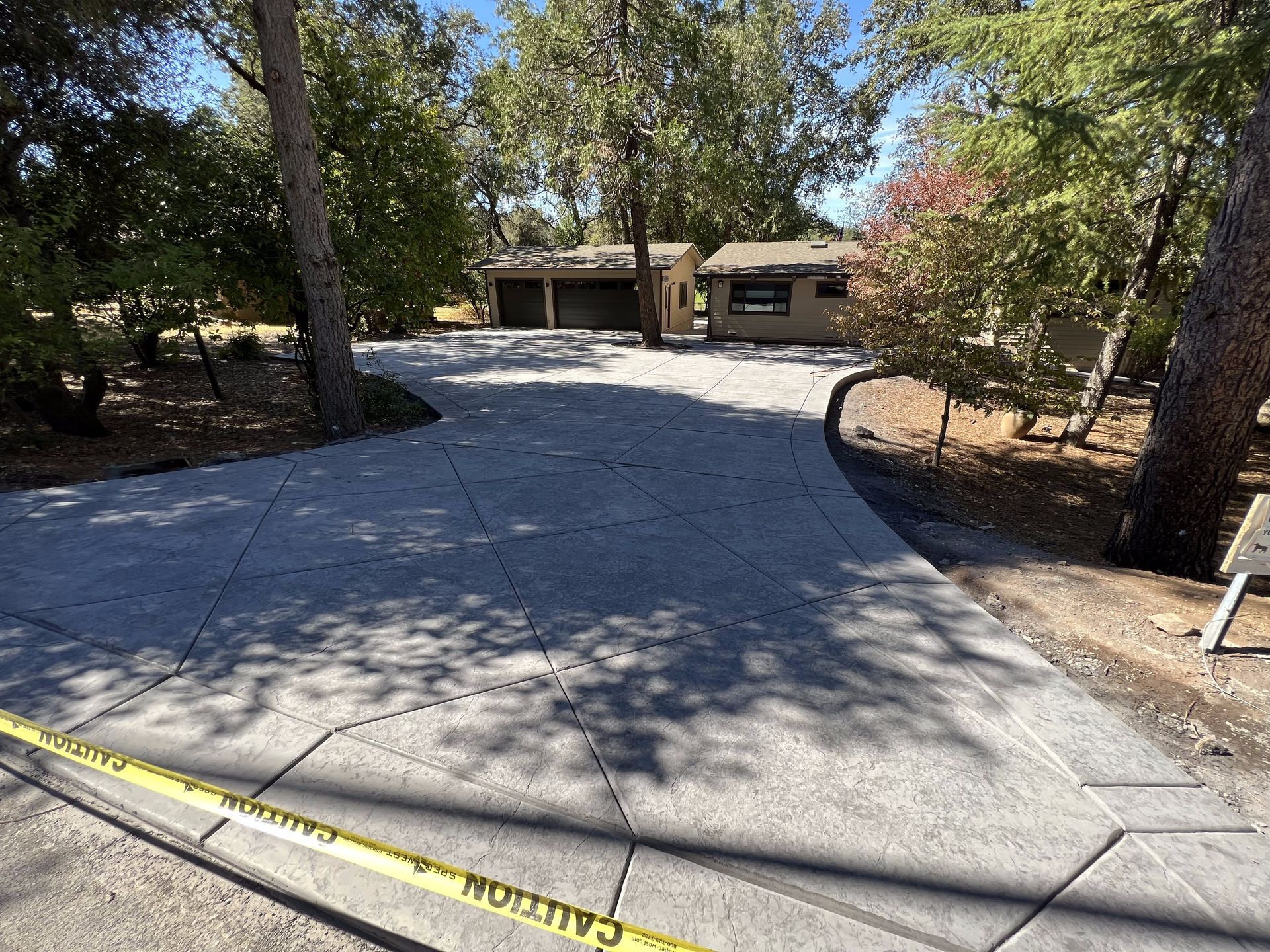 A concrete driveway leading to a house with trees in the background.