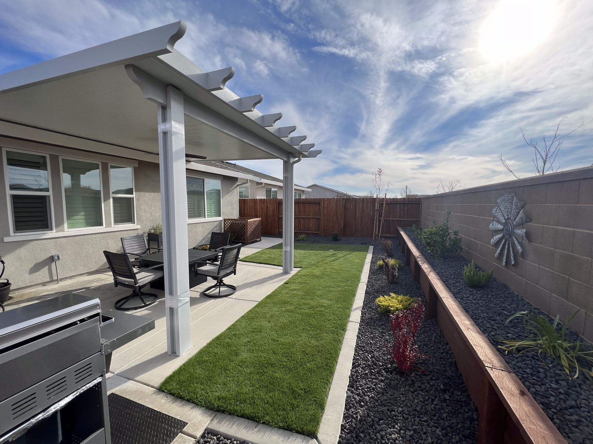 A patio with a grill and a pergola in the backyard of a house.