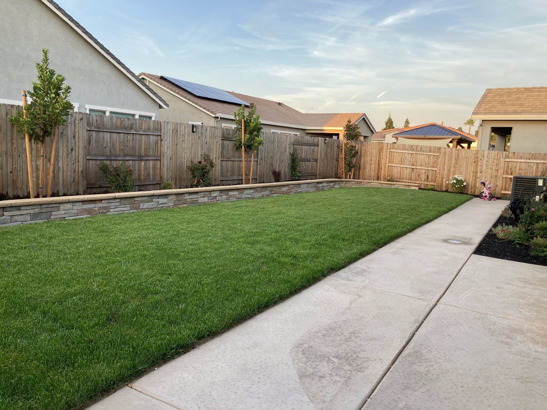 A backyard with a wooden fence and a concrete walkway leading to it.