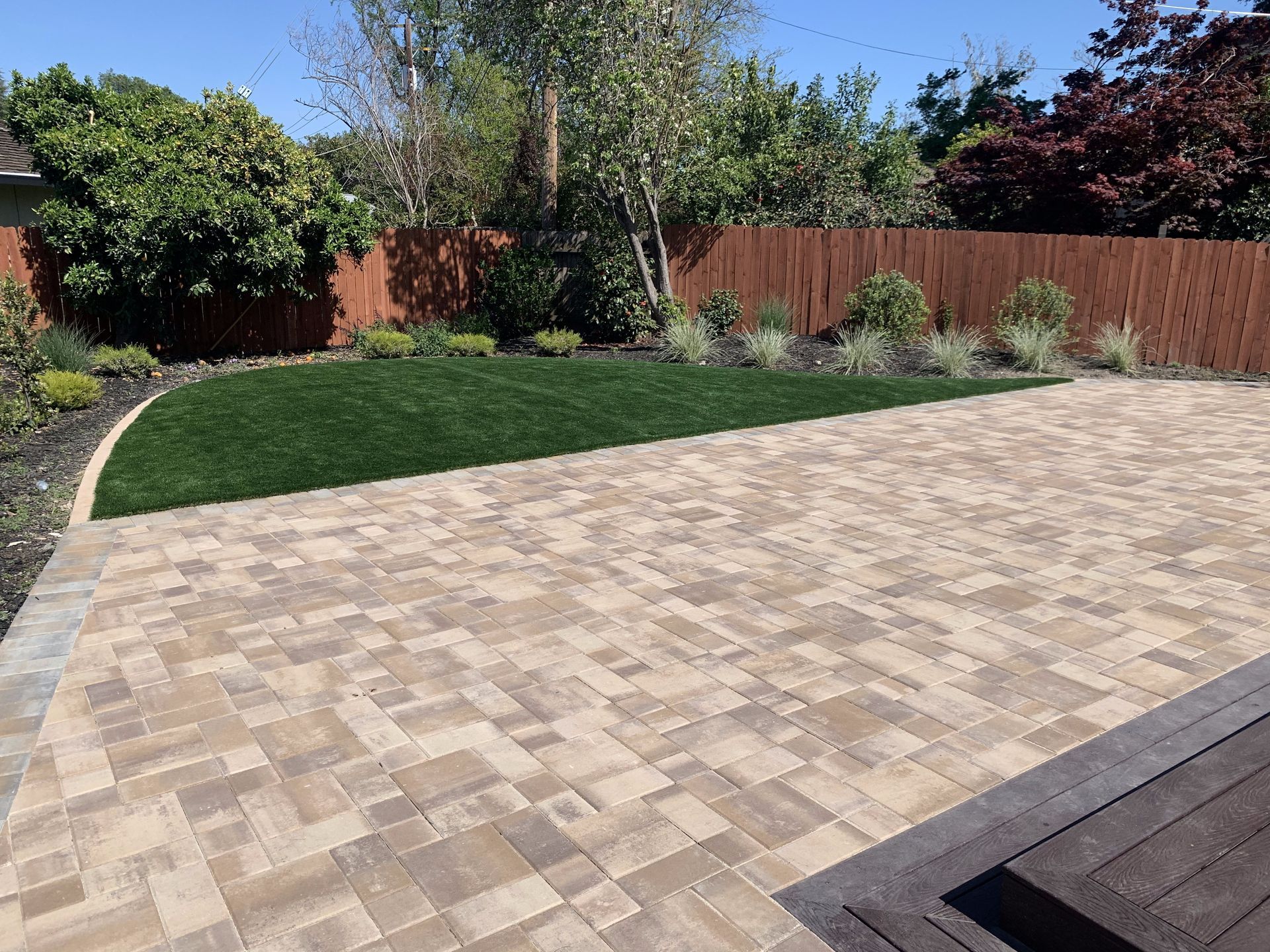 A backyard with a brick driveway and a wooden fence.