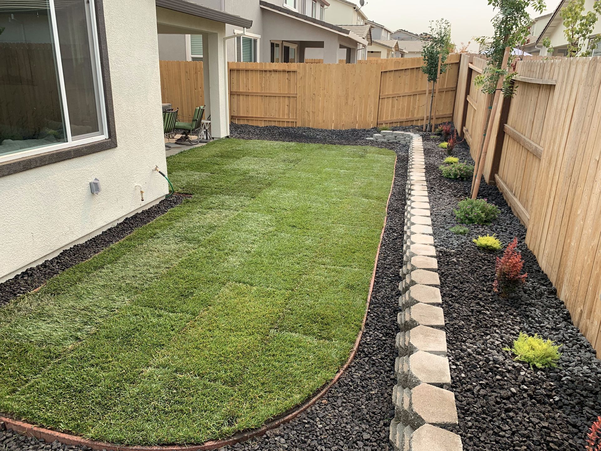 A backyard with a wooden fence and a lush green lawn.