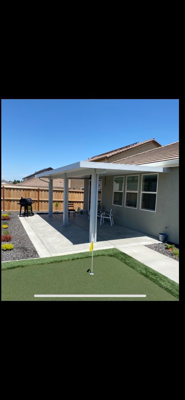 A house with a covered patio and a putting green in front of it.