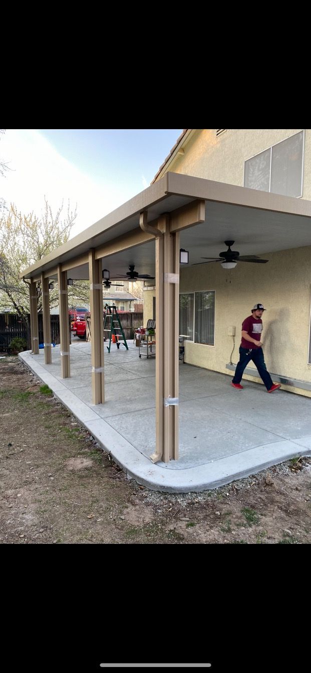 A man is standing under a covered patio in front of a house.