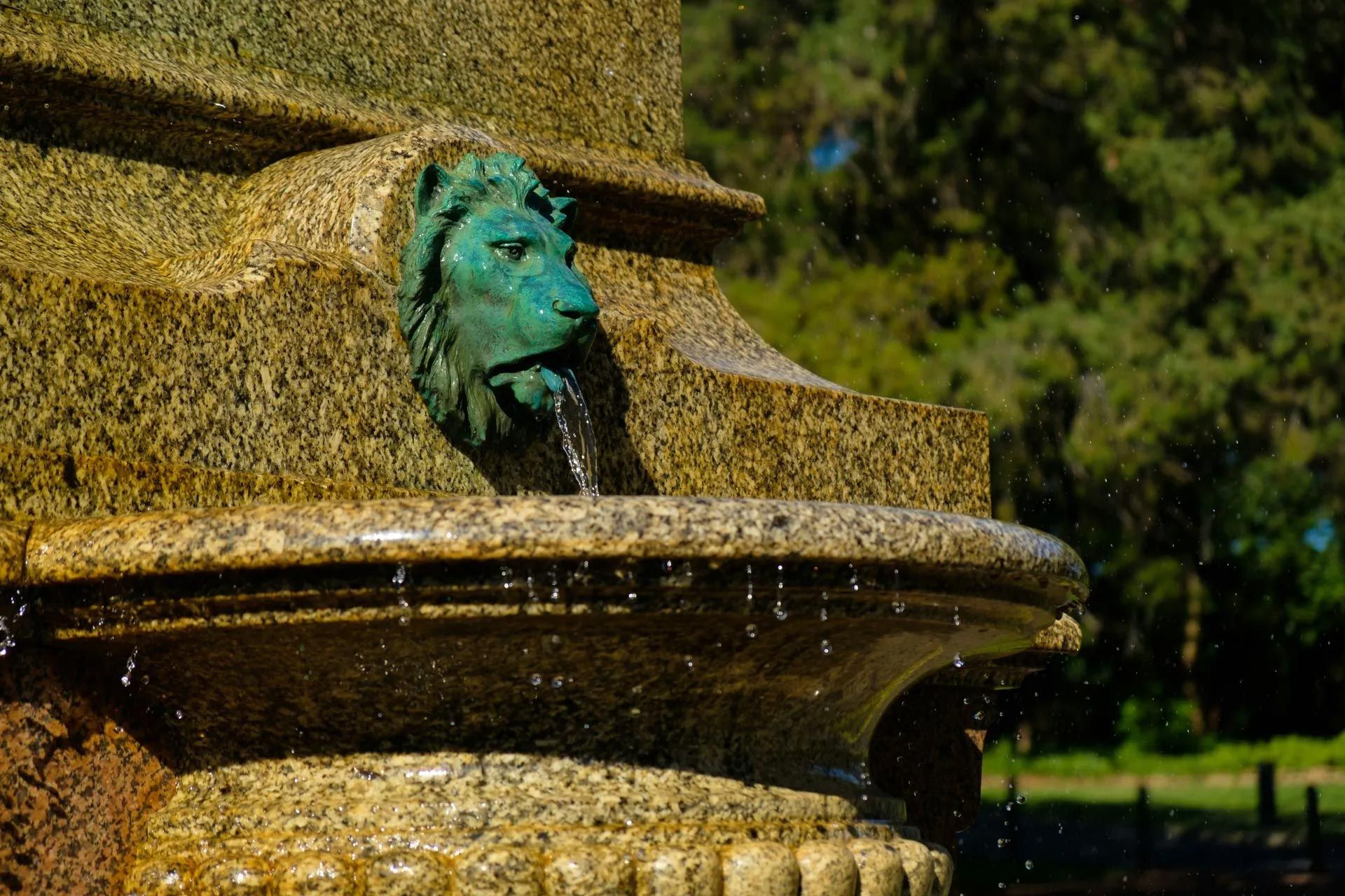 Lion head fountain, water cascading into a stone basin.