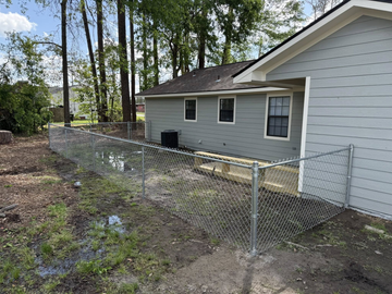 A chain link fence is surrounding the backyard of a house.