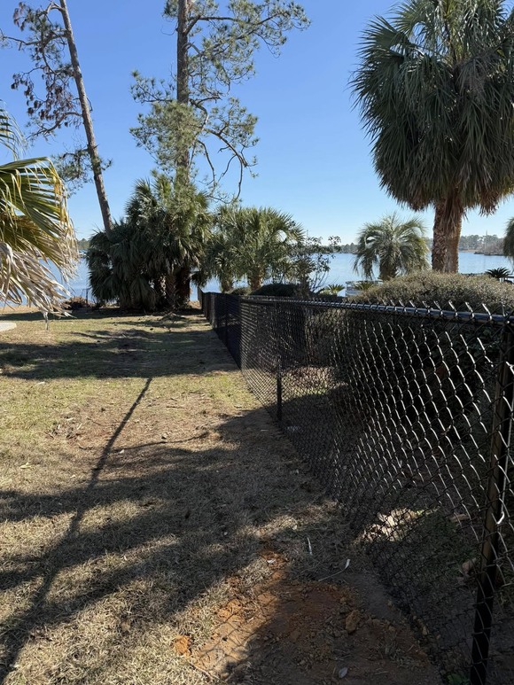 A chain link fence surrounds a yard with trees and a body of water in the background.