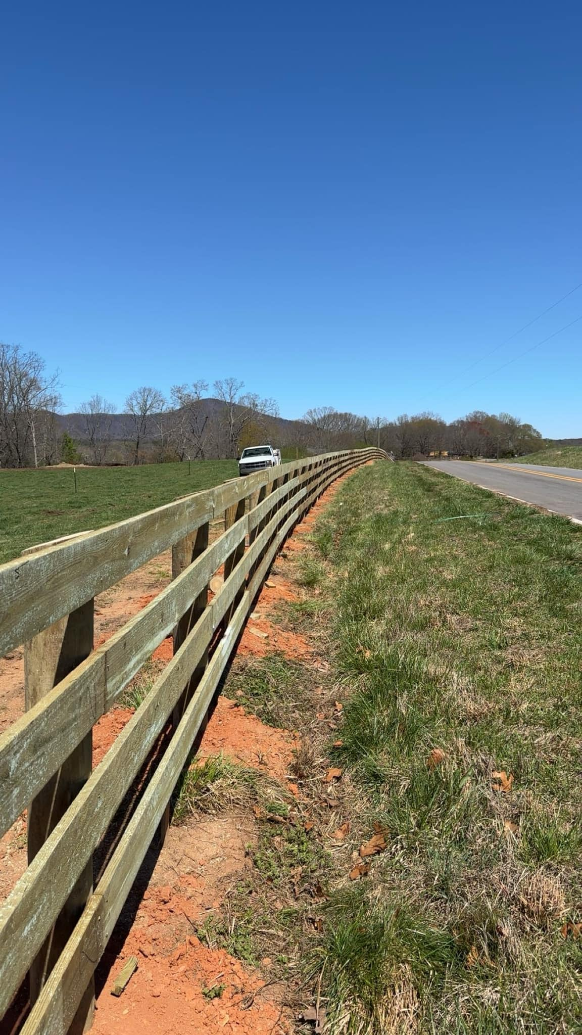 A wooden fence along the side of a road in a field.