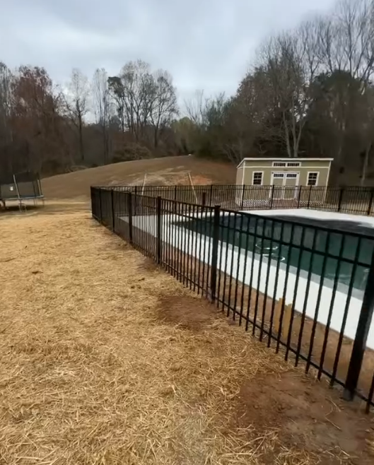 A black metal fence surrounds a large swimming pool.