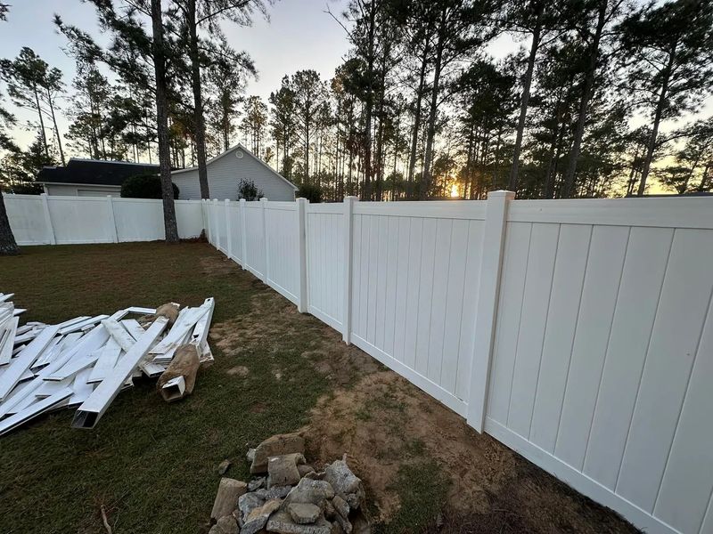 A white vinyl fence is in the backyard of a house.