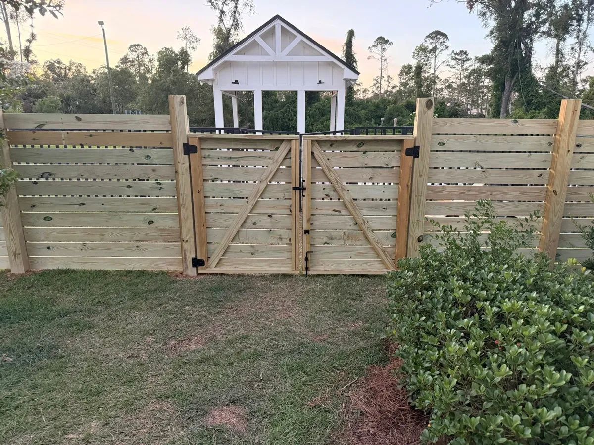 A wooden fence with a gate in front of a small white house.