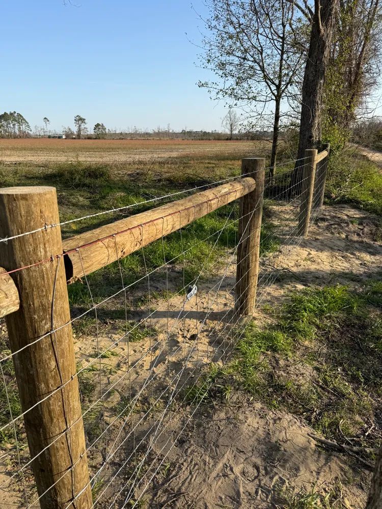 A wooden fence with barbed wire surrounding a field.
