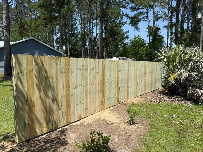 A wooden fence is surrounded by trees in a yard.