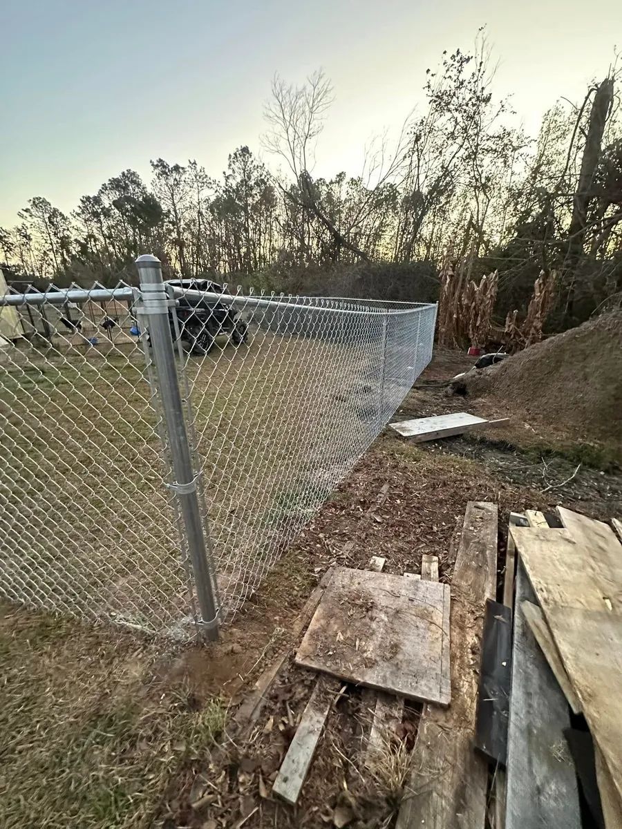 A chain link fence is sitting on top of a dirt hill next to a pile of wood.