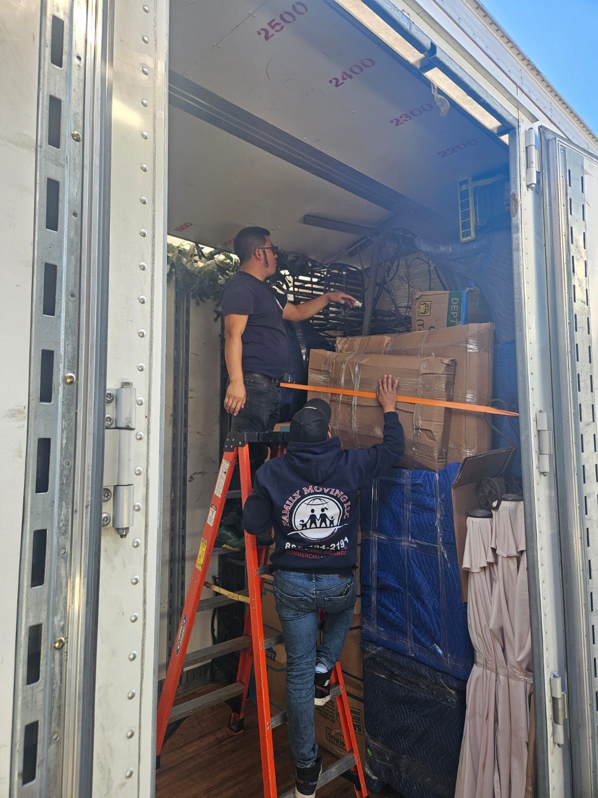 Two men are standing on a ladder in the back of a truck.