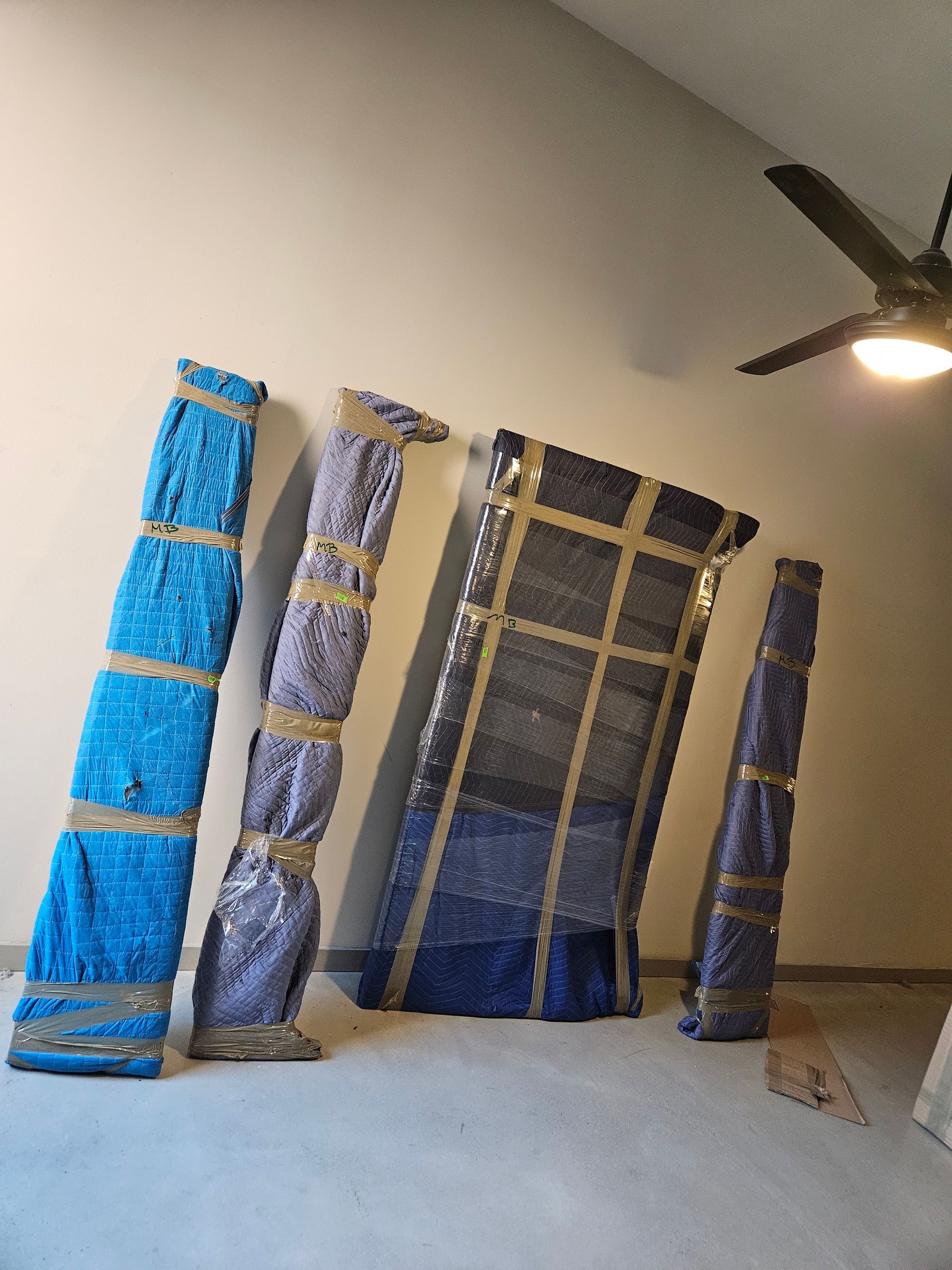 A room with a ceiling fan and a few pieces of furniture wrapped in plastic.