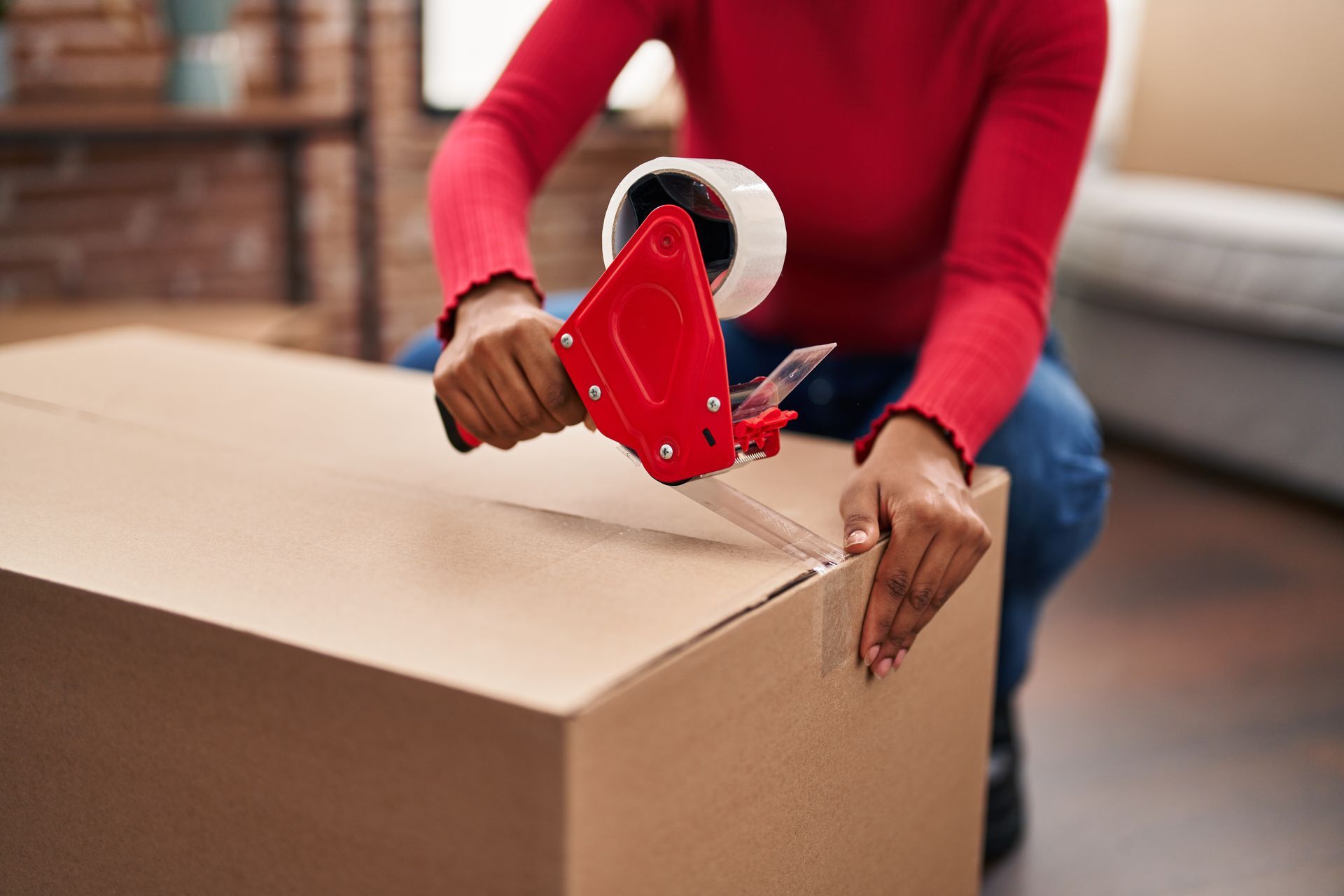 A woman is taping a cardboard box with tape.