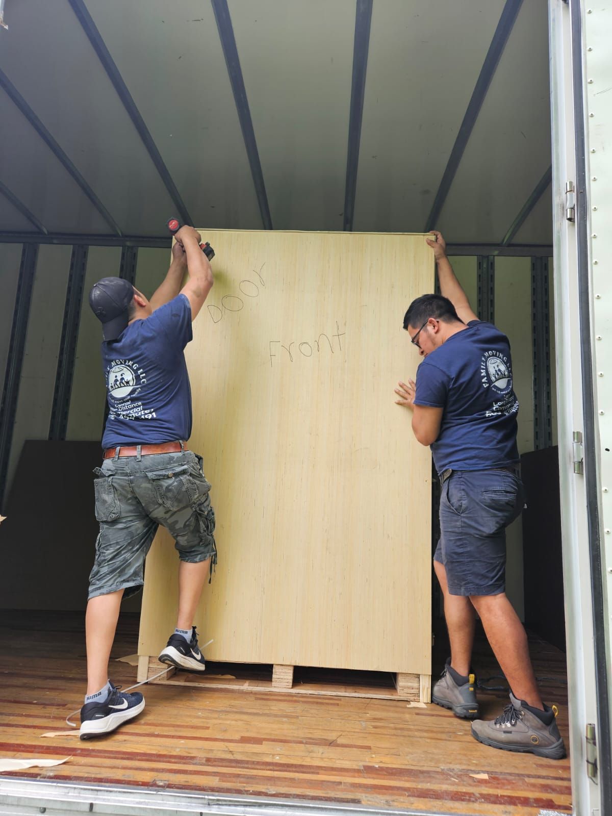 Two men are lifting a large piece of wood in a truck.