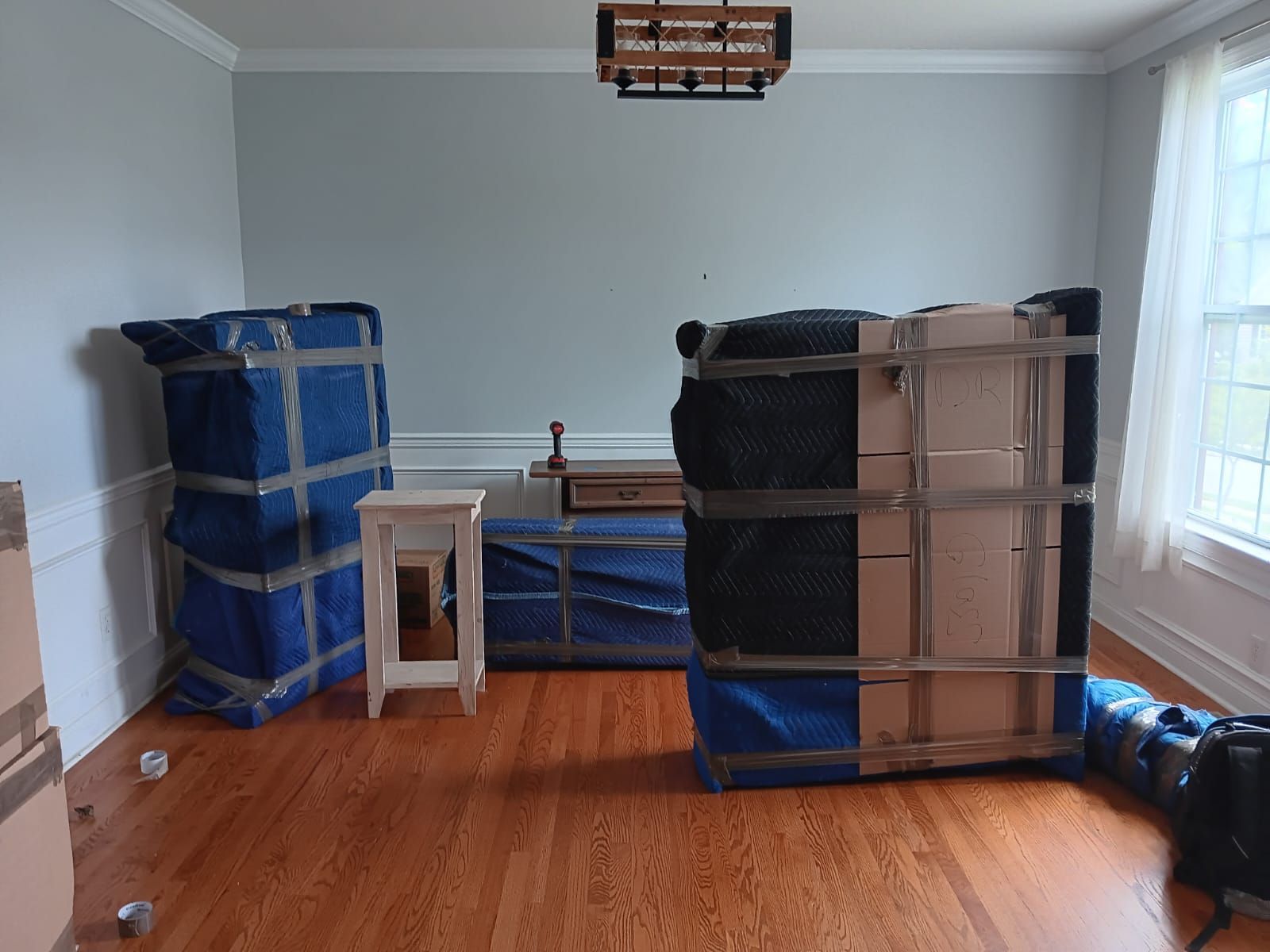 A living room filled with boxes and furniture wrapped in blue tape.