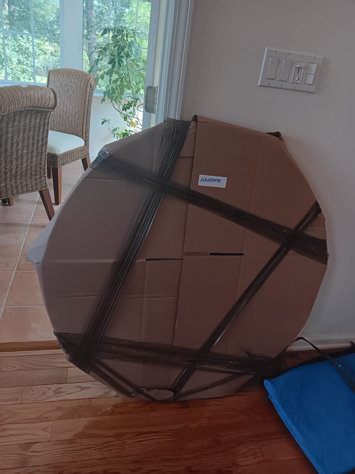 A round cardboard box wrapped in black tape is sitting on a wooden floor.