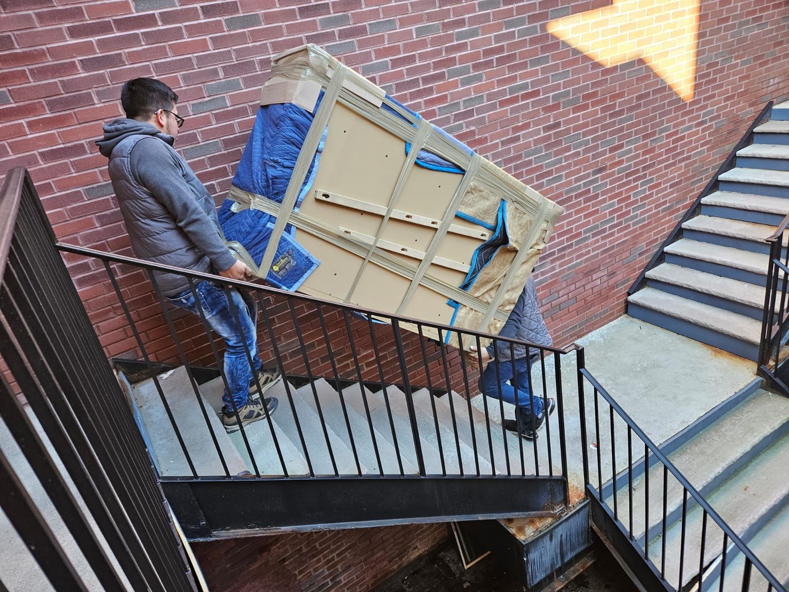 Two men are carrying a piano up a set of stairs.