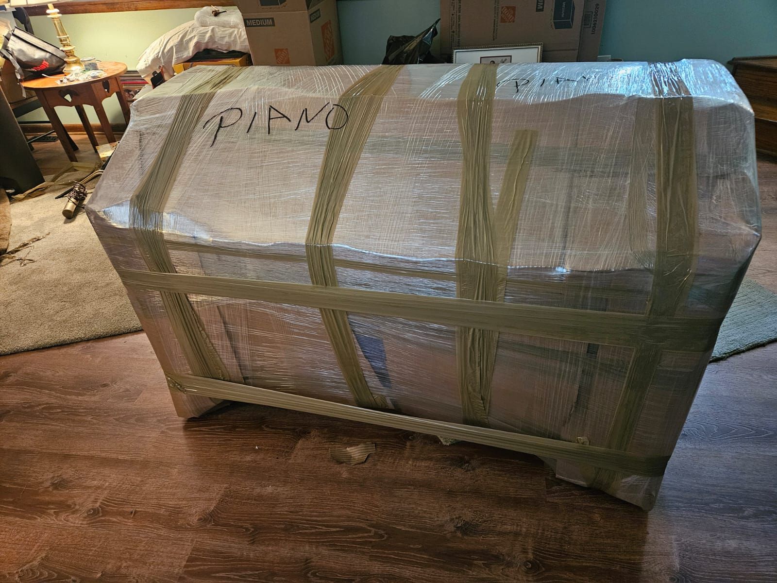 A piano is wrapped in plastic and tape in a room.
