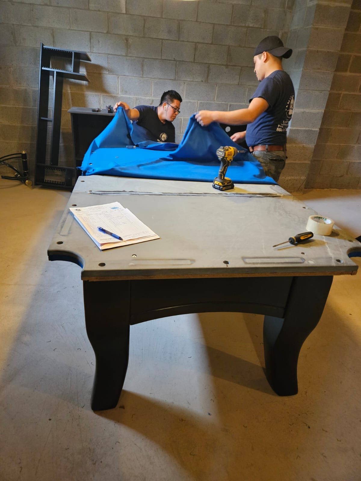 Two men are working on a pool table in a basement.