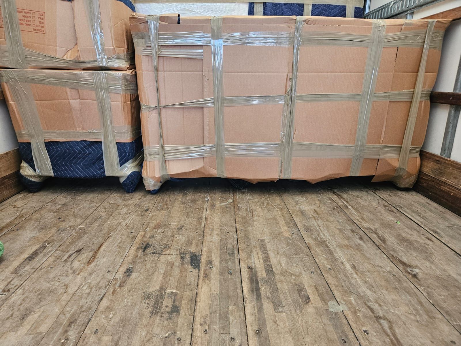Two cardboard boxes wrapped in tape are sitting on a wooden floor.